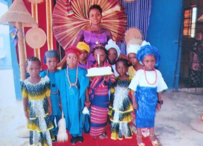 Nursery pupils in traditional outfits standing before a woven backdrop with a cake